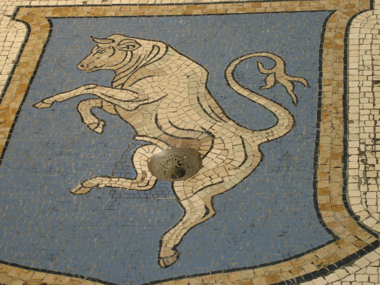 A bull, made of tile, in the floor at the center of the mall.  The hole has been caused by...