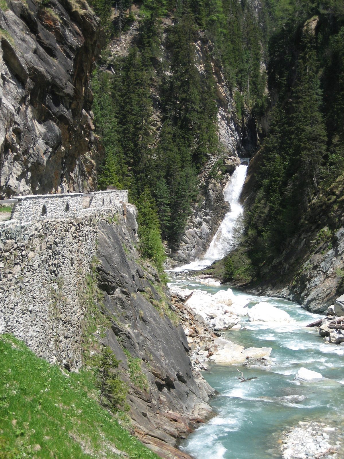 The river, a waterfall into it, and the stone wall on the side of the hiking path