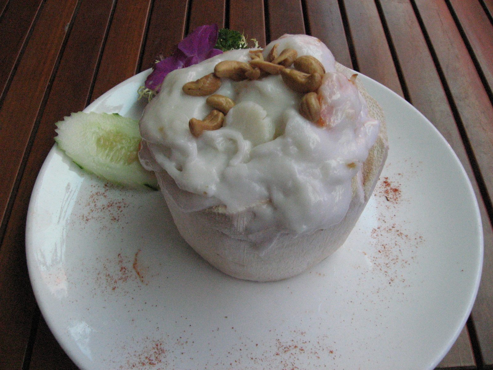 Baked seafood rice dish served inside a coconut with coconut milk based sauce (and peanuts) on...
