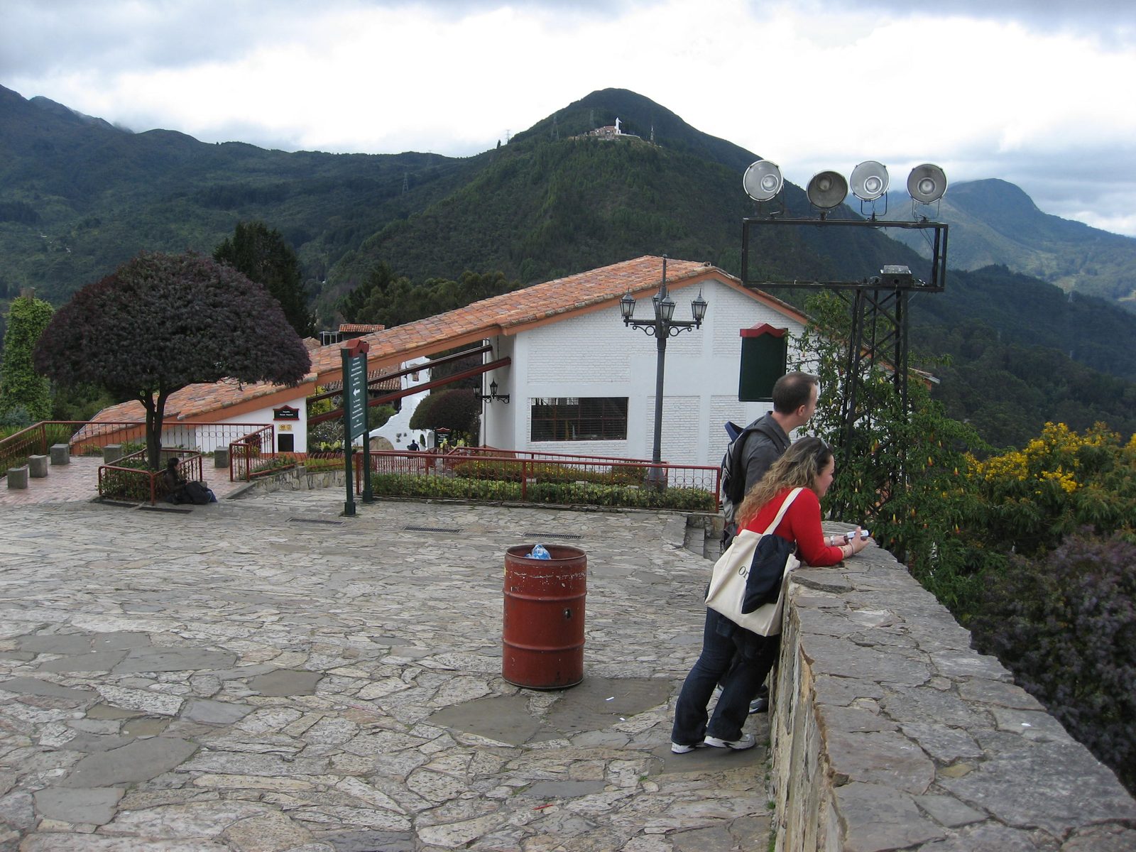 Some tourists gaze out at the city.  A large statue of some monk or friar is on the hill in the...