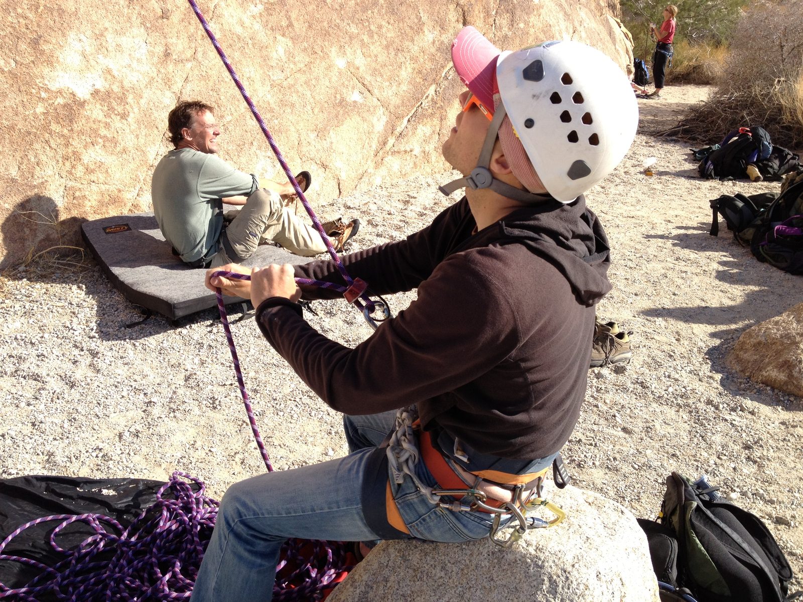 John, belaying from a rock while Jim puts on some shoes on a bouldering pad.