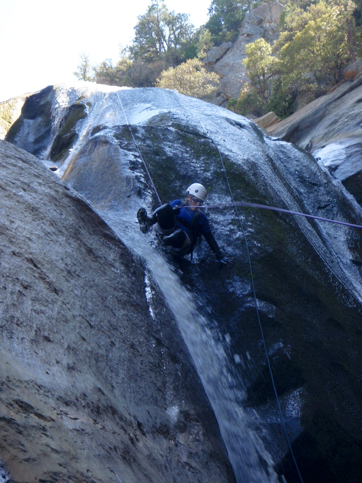 Catherine rappelling down through a waterfall, sliding on her hip.
