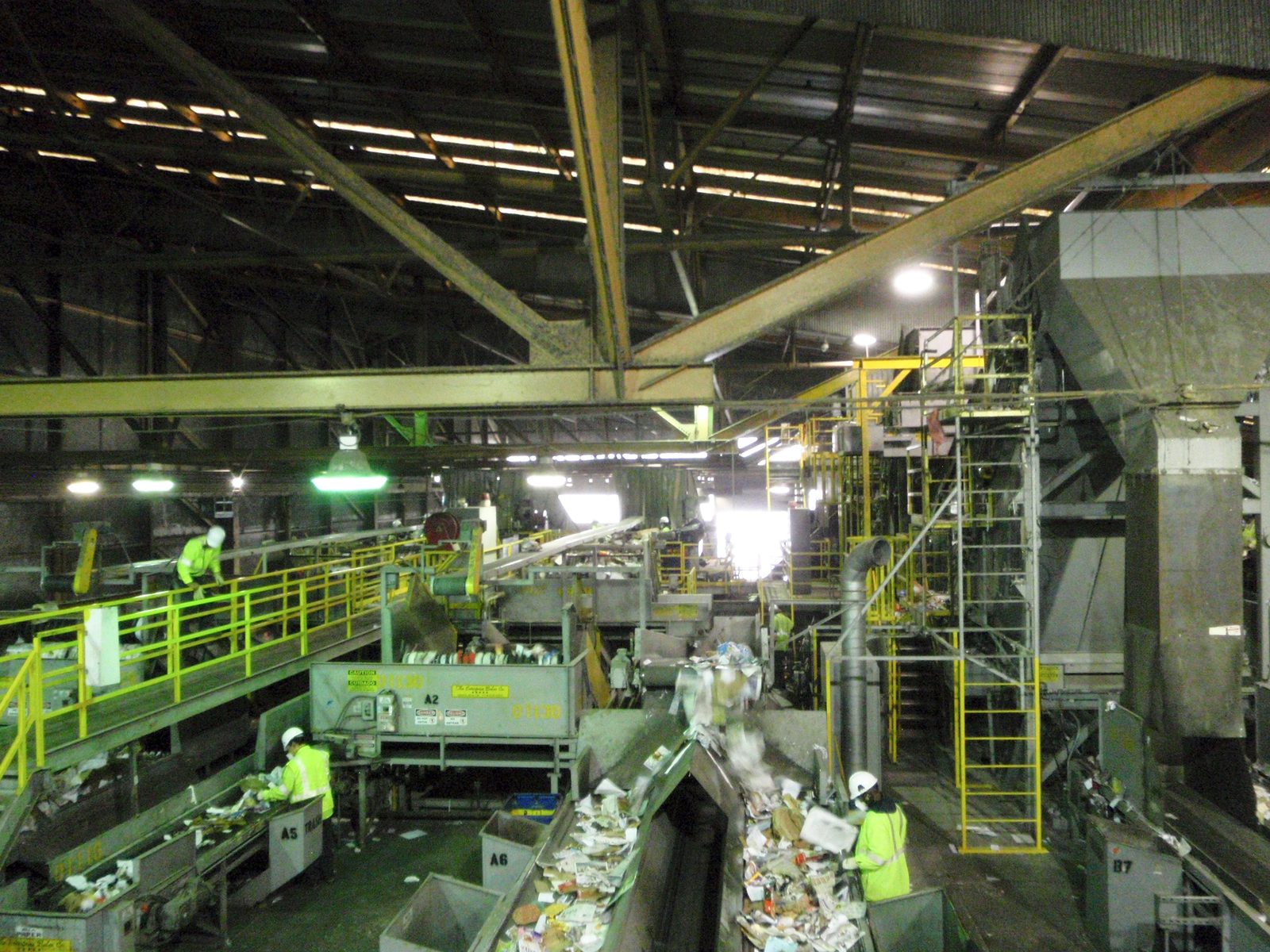 Workers manually pick out plastic and metal from a predominantly paper and cardboard waste stream.