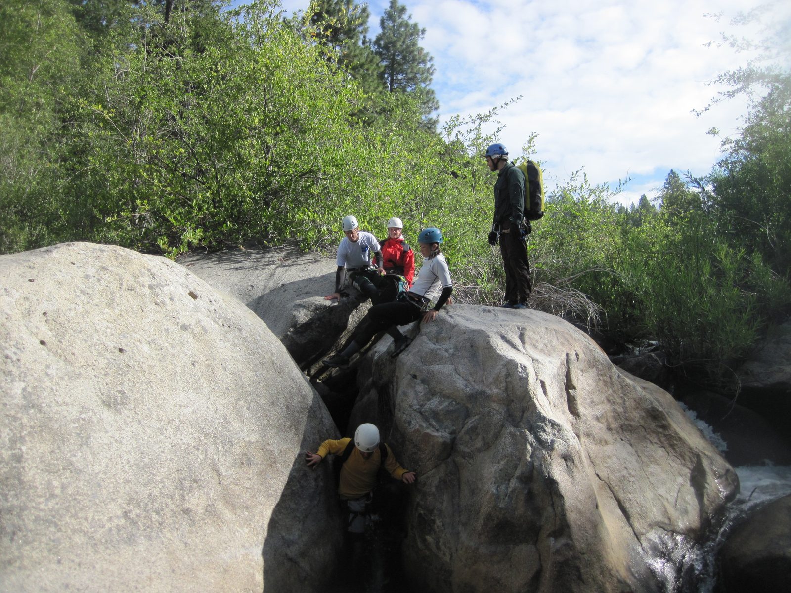 Eliah works through a bouldering problem while Tracy, Ben, Jill, and Joel look on.