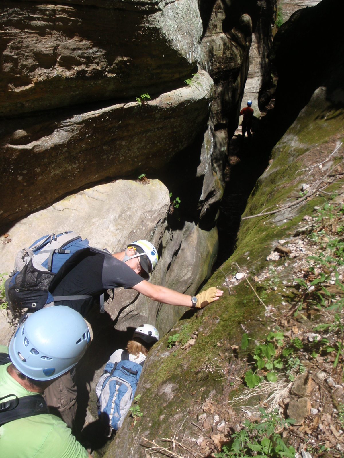 Meredith downclimbs into a narrow slot filled with dark water, while Andy and Mike watch.