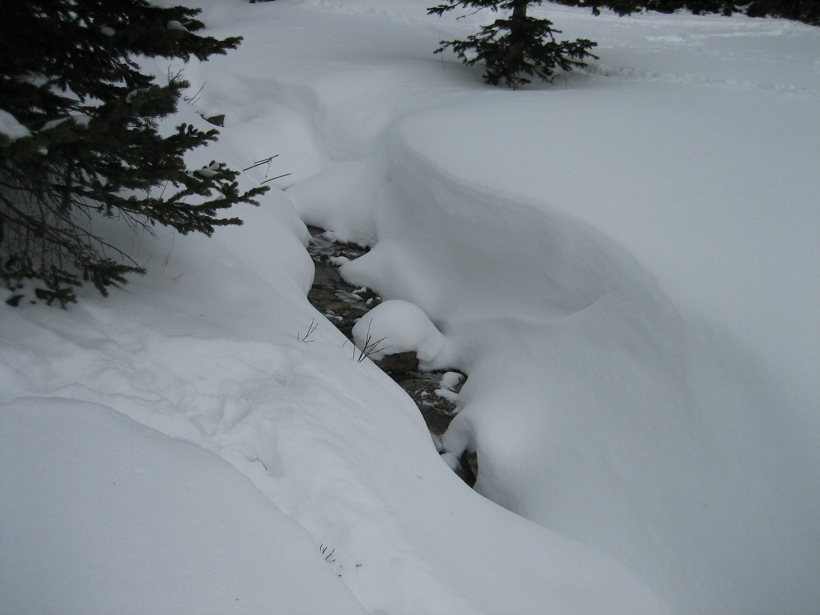 The Beehive Basin drainage peeking out between windblown snowbanks.