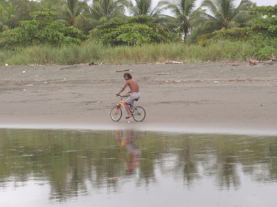 Guy riding his bicycle rather impressively in wet sand.