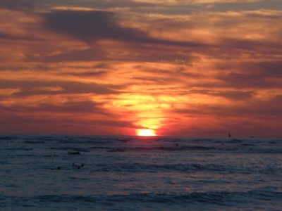 More surfers watching the sunset between waves on Waikiki Beach.