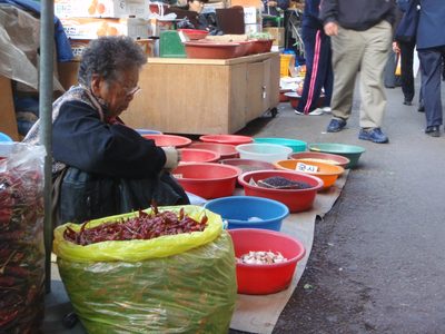 Woman selling spices and specialty grains on the sidewalk.