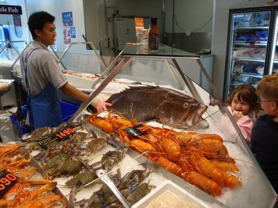 A fishmonger showing off a fish to some admiring Aussie children.