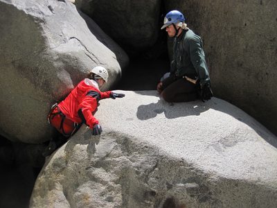 Joel watching as Jill climbs up a boulder to enter a...