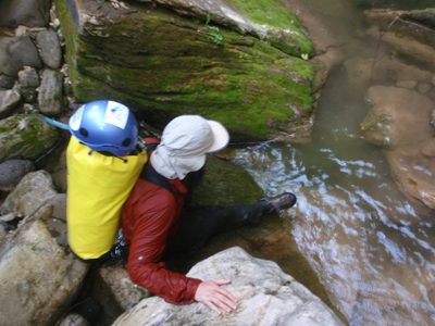 Joel slides down a moss-covered smooth rock into a...